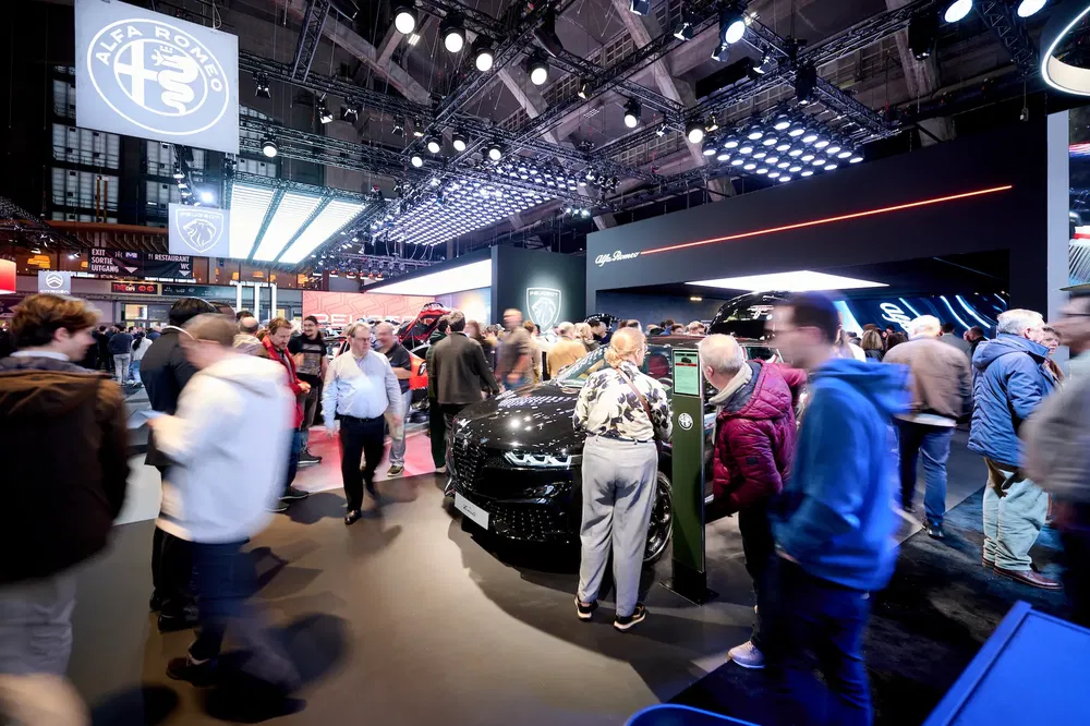 Foule au salon de l'auto autour d'un stand Alfa Romeo moderne et éclairé.