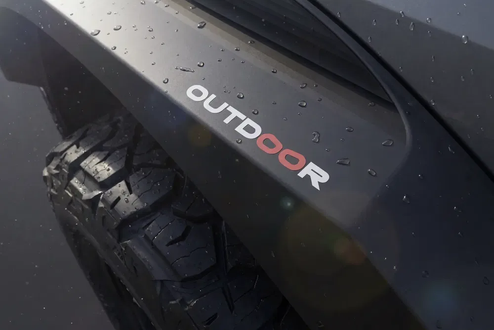 Zijkant van een auto met 'OUTDOOR'-sticker en stevige banden in de regen.
