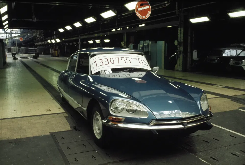 Citroën DS bleu sur chaîne de montage avec panneau marquant la production en série.