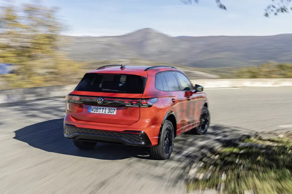 Achteraanzicht van rode Volkswagen SUV op kronkelige bergweg.