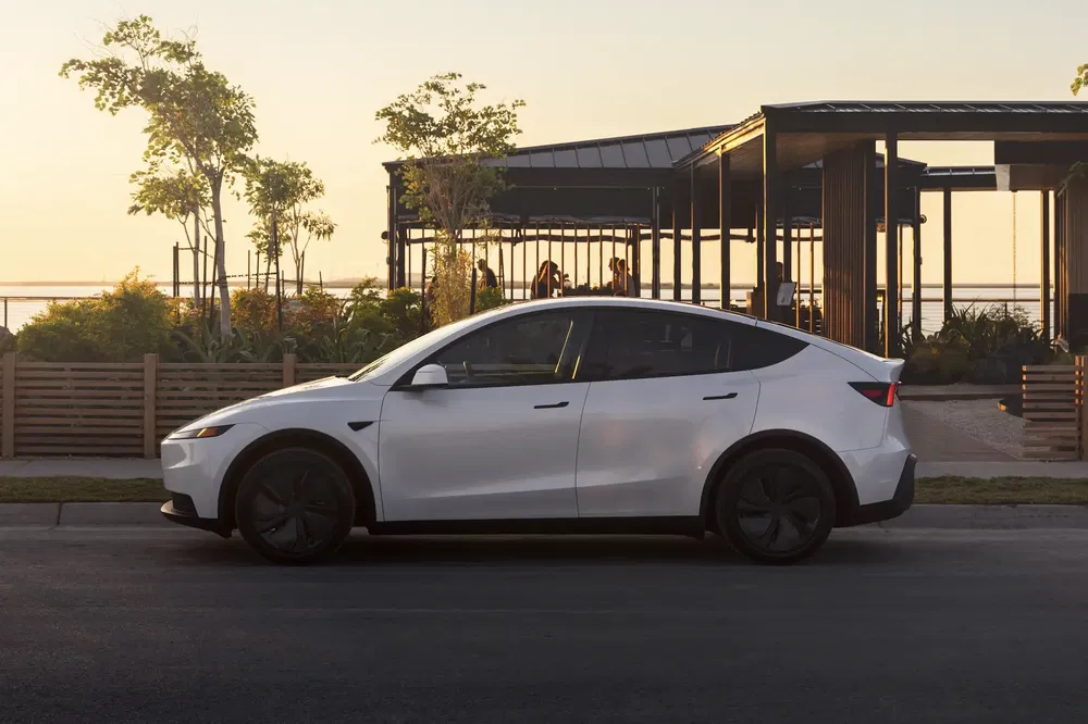 Witte Tesla Model Y geparkeerd voor een modern paviljoen bij zonsondergang.