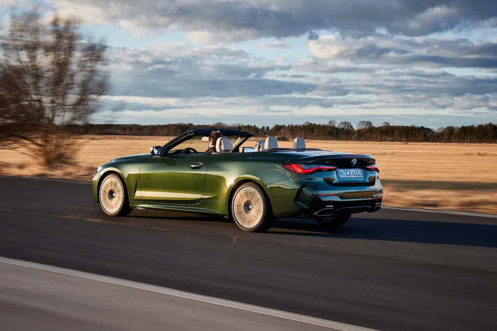 BMW Série 4 Cabriolet verte roulant sur une route dégagée, ciel nuageux en arrière-plan.