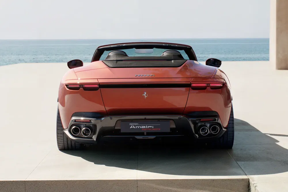 Rode Ferrari Roma Spider aan zee, elegante sportieve achterkant.