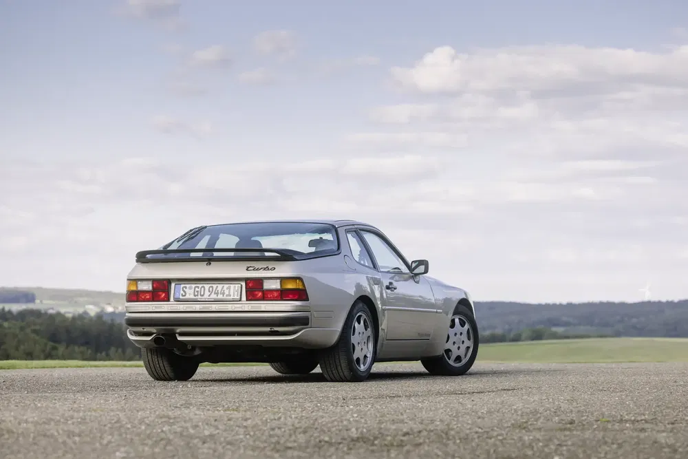Porsche 944 Turbo gris stationné sur une route, ciel dégagé en arrière-plan.