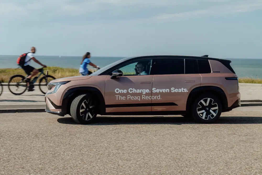 Voiture électrique HiPhi sur route côtière avec cyclistes à l'arrière-plan.