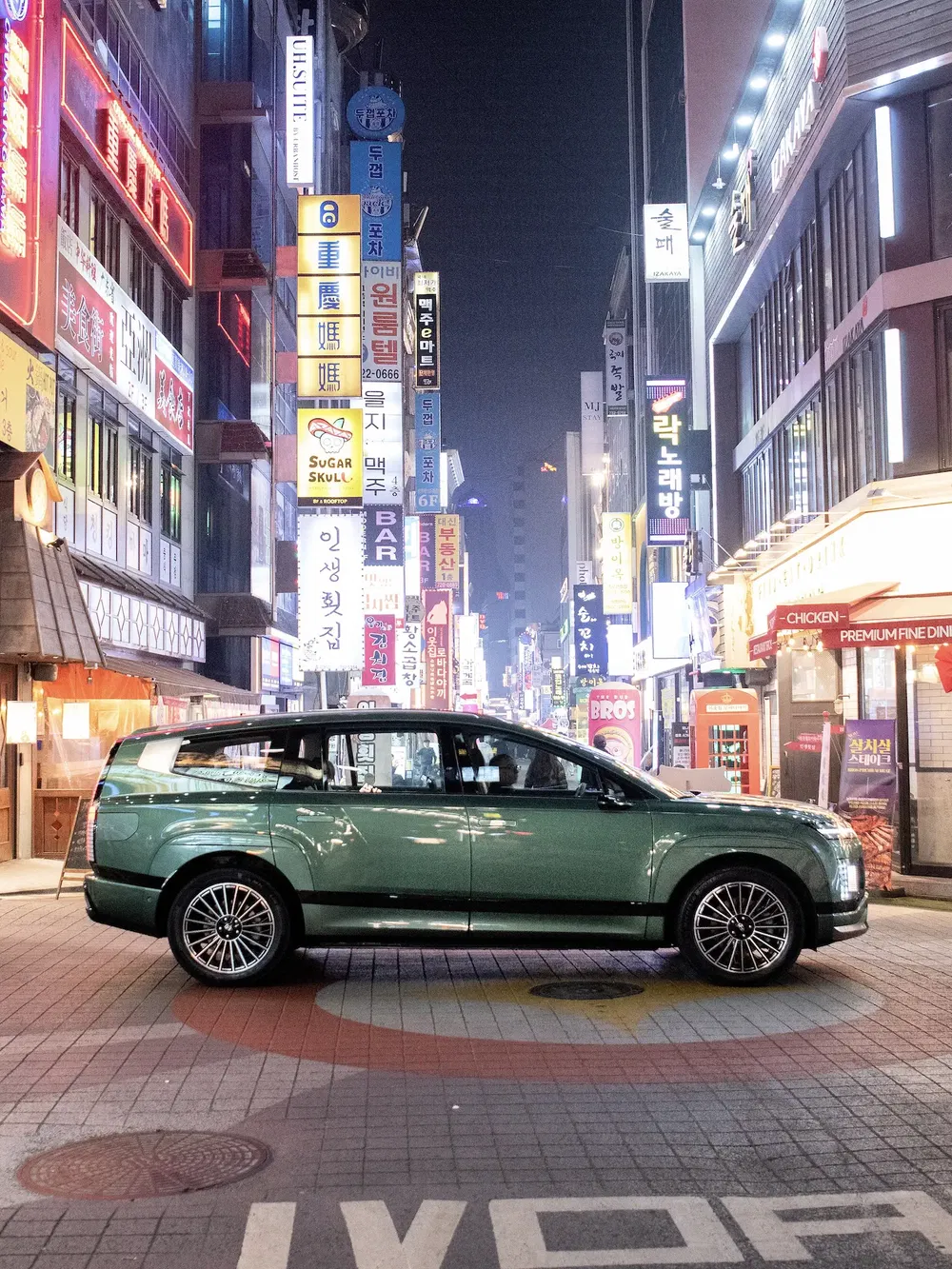 SUV stationné dans une rue lumineuse de Séoul, panneaux publicitaires coréens visibles.