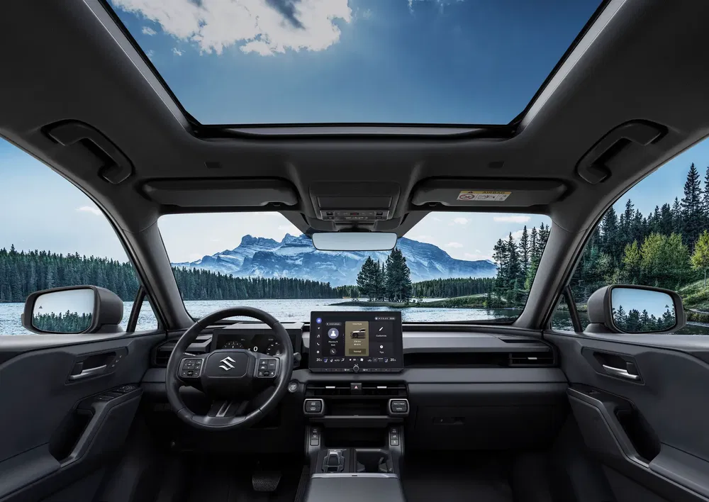 Intérieur du Suzuki avec écran tactile, vue sur un lac et montagnes par le toit panoramique.