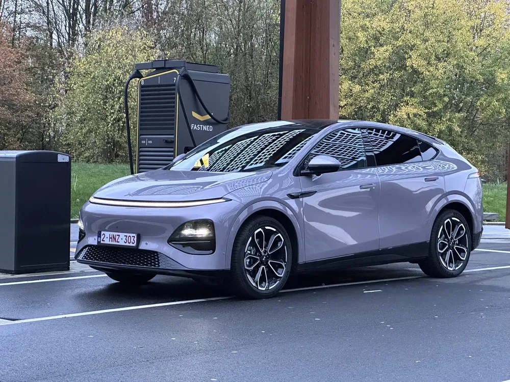 SUV électrique Fastned gris argenté en charge sur une station moderne entourée d'arbres.