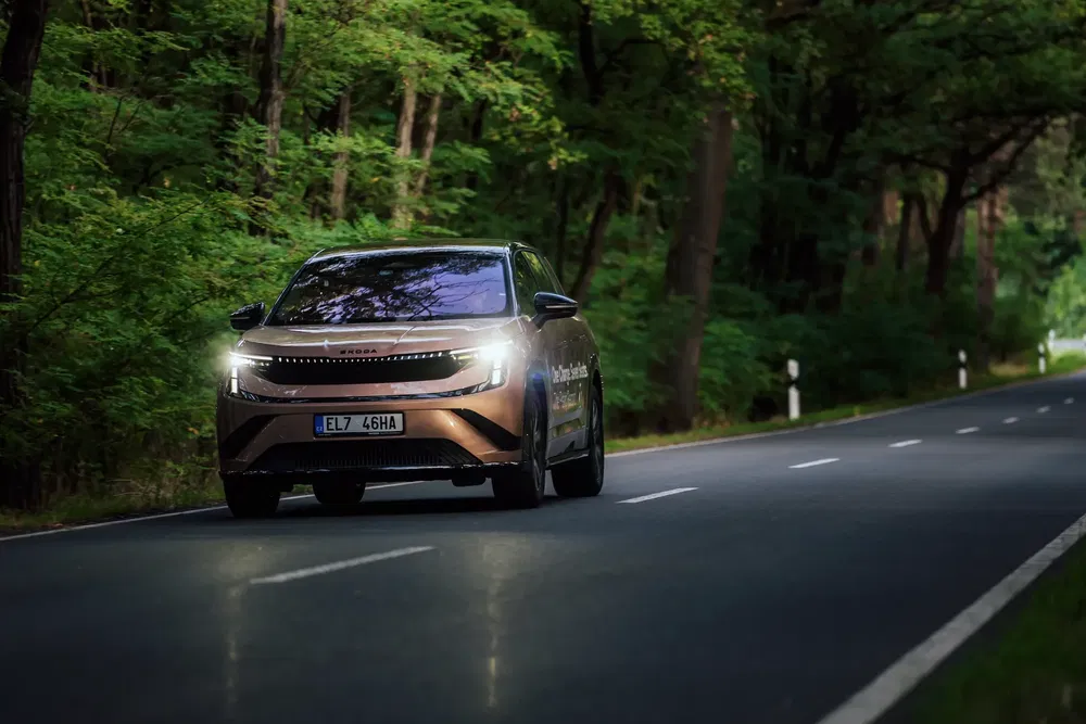 Škoda Enyaq roulant sur une route forestière avec phares allumés.