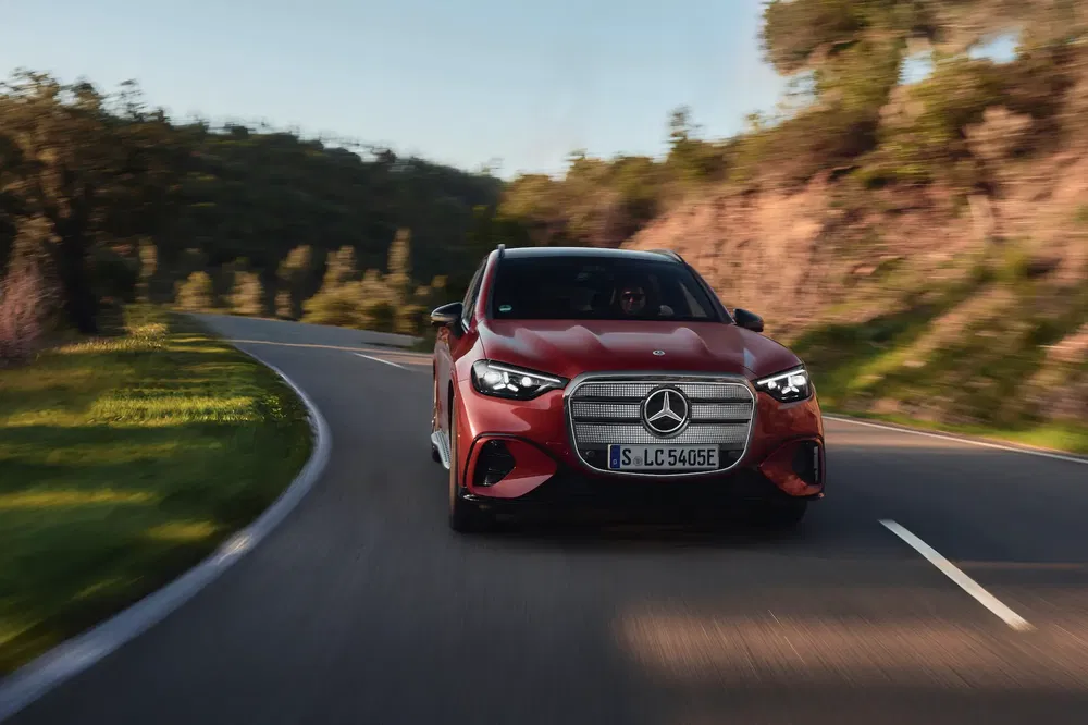 Rode Mercedes auto op kronkelende weg, natuur op de achtergrond, zonnige dag.