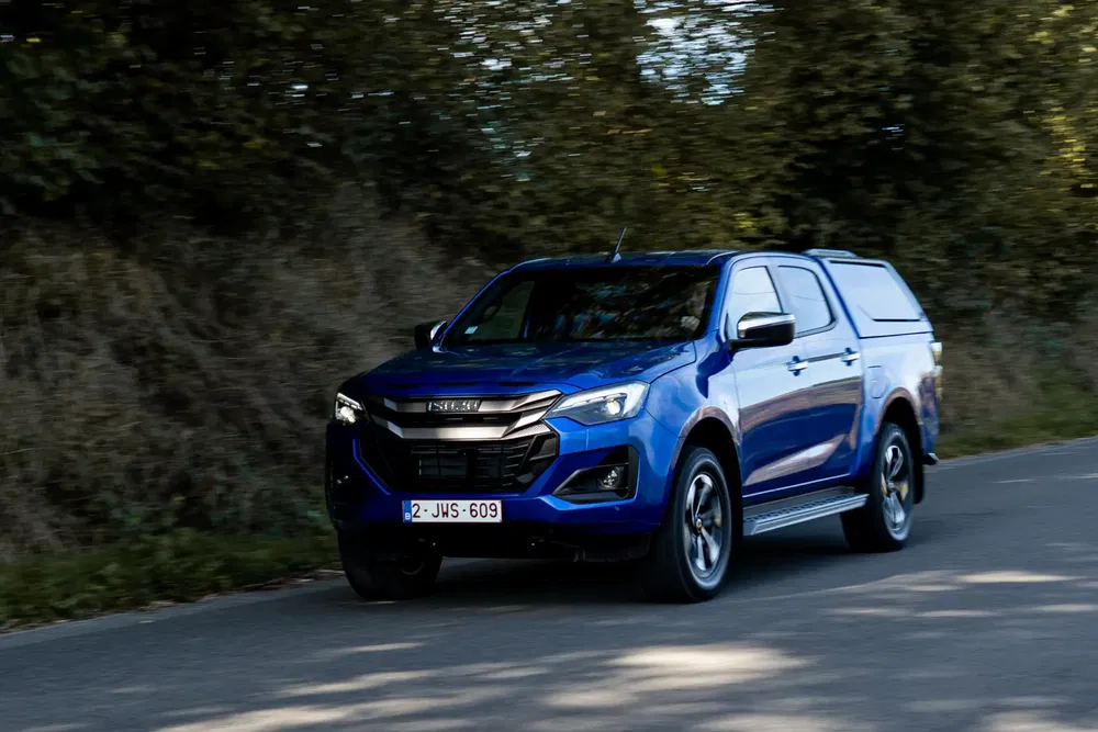 Isuzu D-Max bleu roulant sur une route, entouré de verdure et d'arbustes.