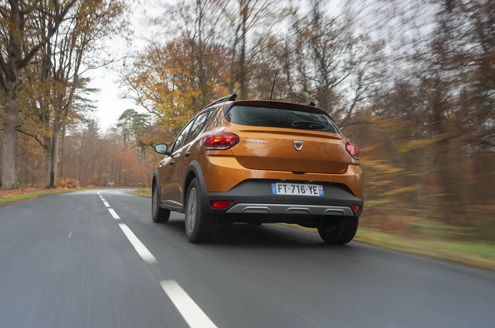 Bruine Dacia Sandero rijdend op een met bomen omzoomde weg in de herfst.