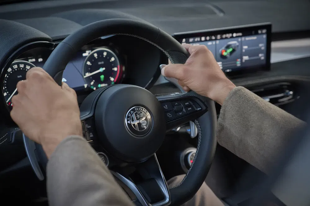 Stuurwiel van Alfa Romeo met modern digitaal dashboard op de achtergrond.