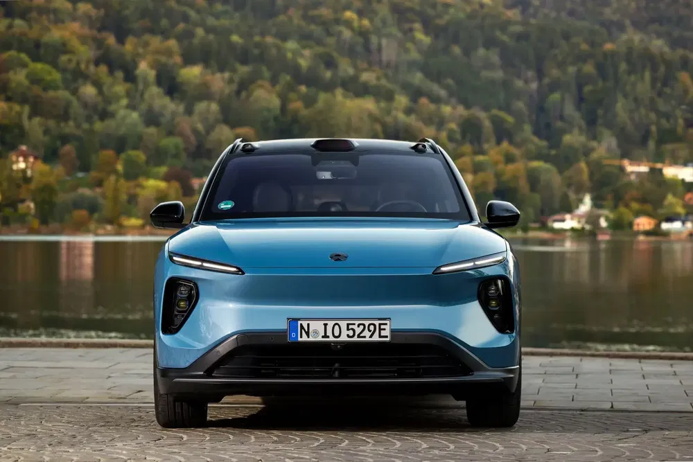 Vooraanzicht van de blauwe elektrische NIO ES8 SUV, geparkeerd bij een schilderachtig meer.