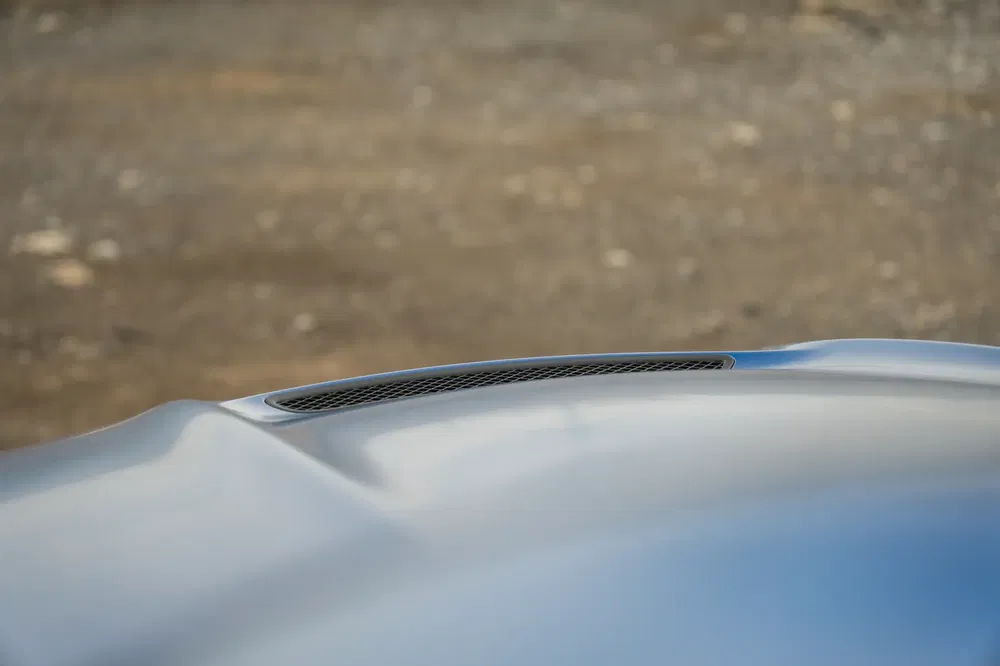 Capot de voiture avec prise d'air intégrée sur fond de route pavée.