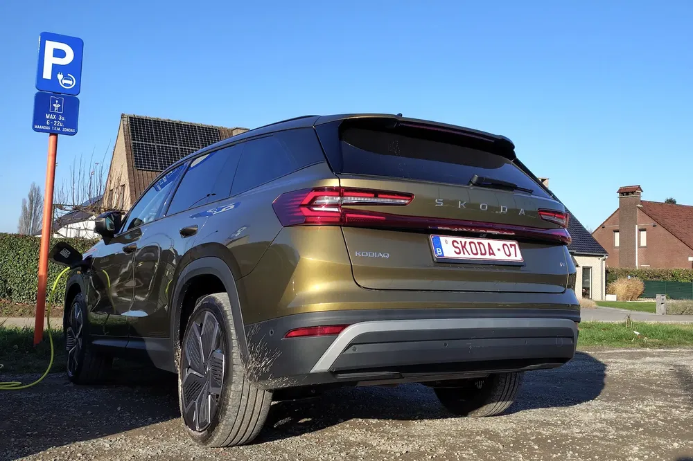 Skoda Kodiaq vert garée près d'une station de recharge avec ciel bleu.