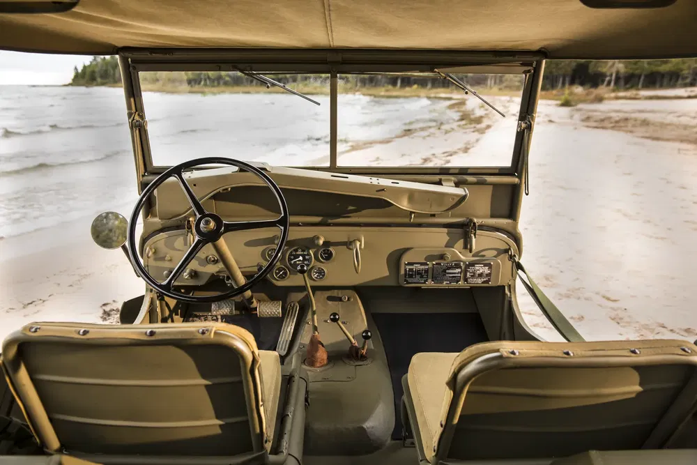 Interieur van een vintage Jeep aan het strand met zwart stuurwiel, minimalistisch dashboard.