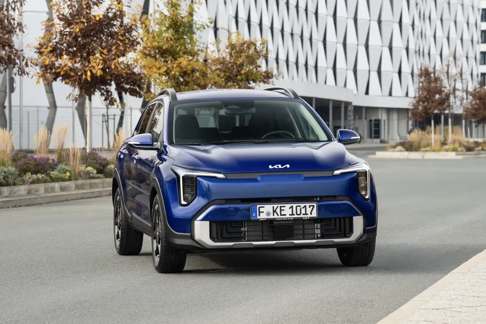 Blauwe Kia SUV geparkeerd voor een modern gebouw met geometrische patronen.
