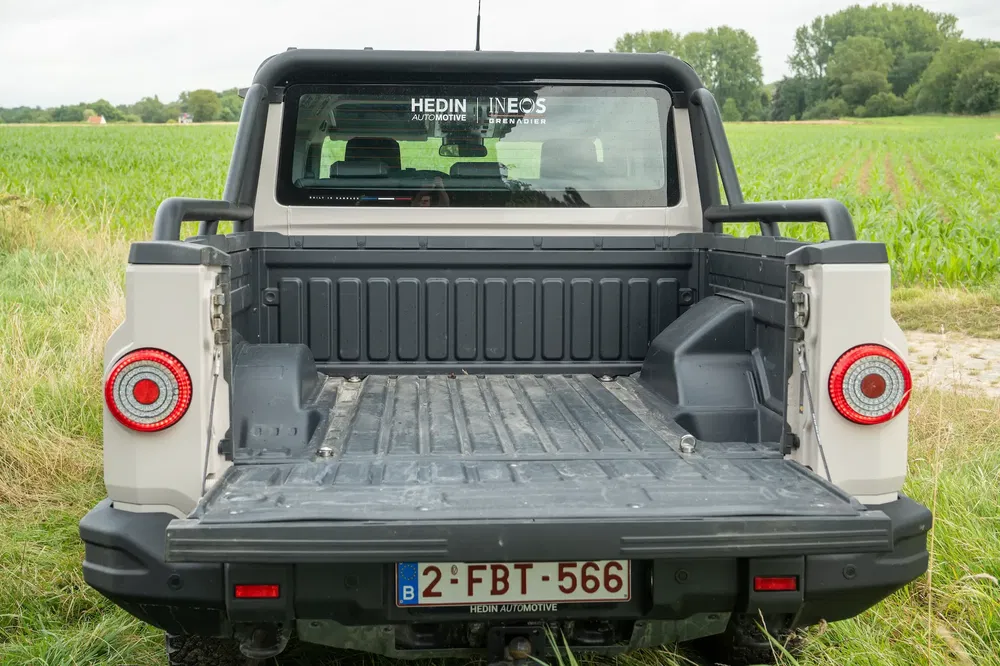 Open laadbak van Ineos Grenadier pick-up in groene landelijke omgeving.