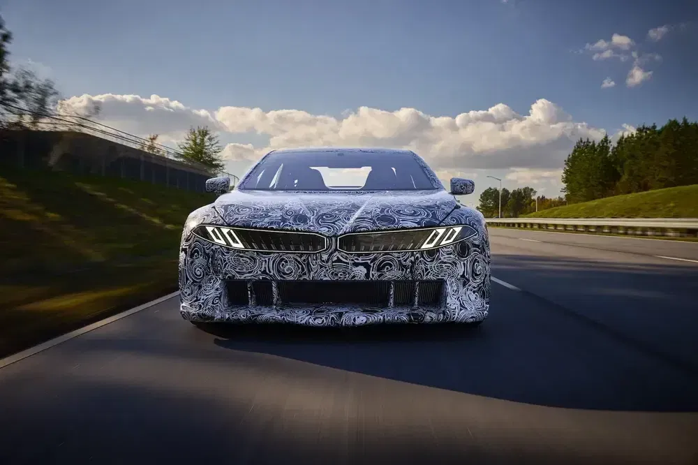 BMW prototype auto testen, zonnige snelweg, blauwe lucht, camouflagedesign.