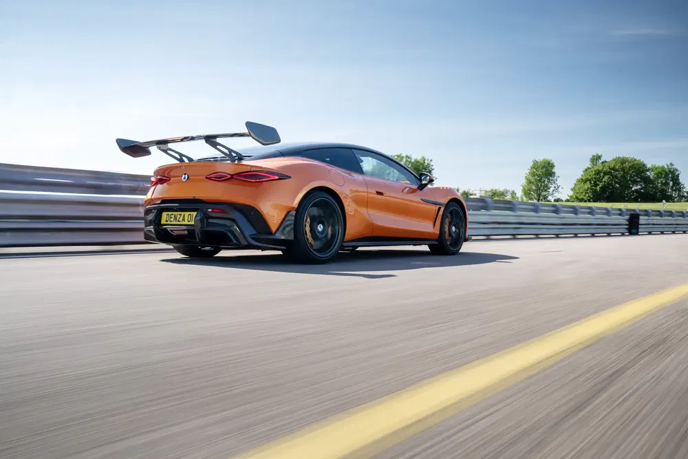 Voiture sportive Denza orange sur piste, aileron arrière proéminent, ciel bleu dégagé.