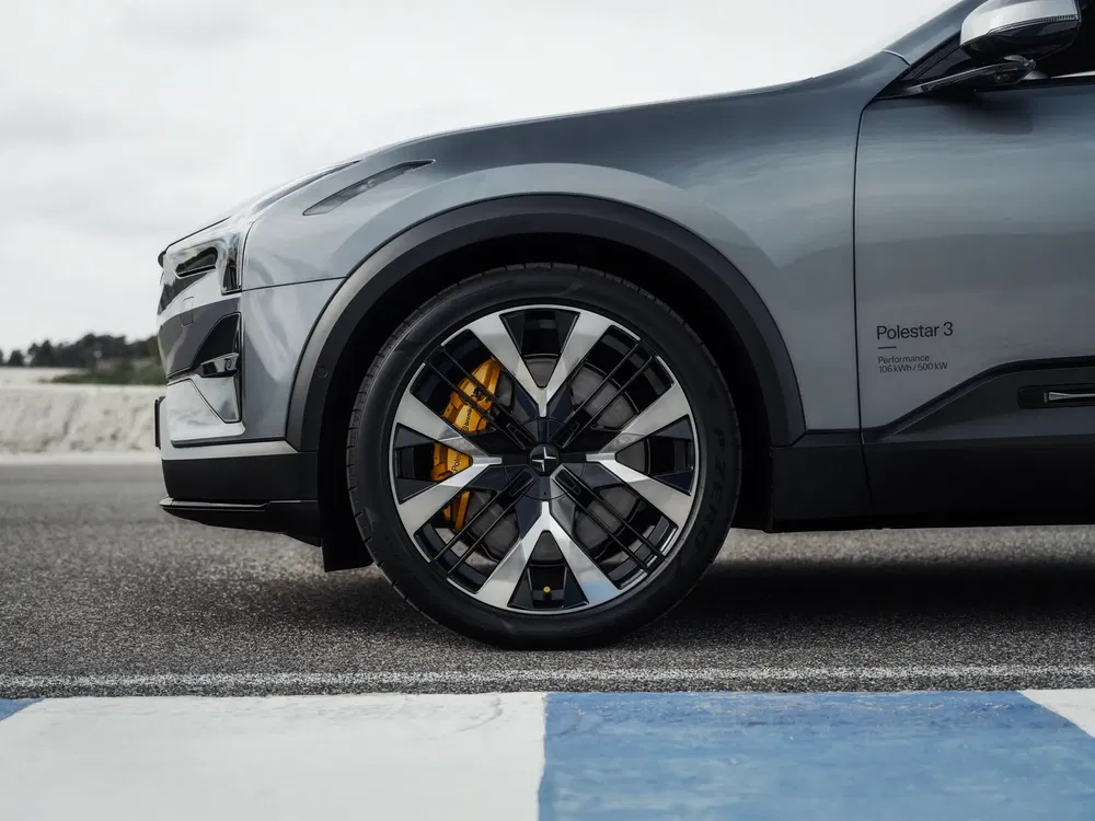 Zijaanzicht van het voorwiel van een grijze Polestar 3 op asfaltbaan.