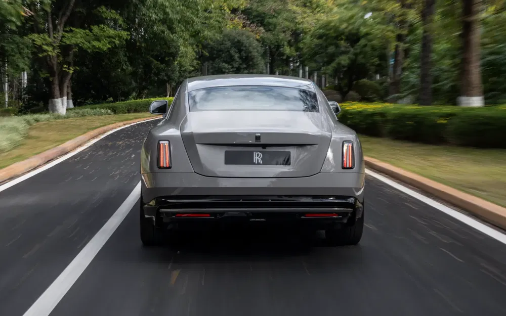 Rolls-Royce gris roulant sur une route bordée d'arbres, vue arrière dynamique.