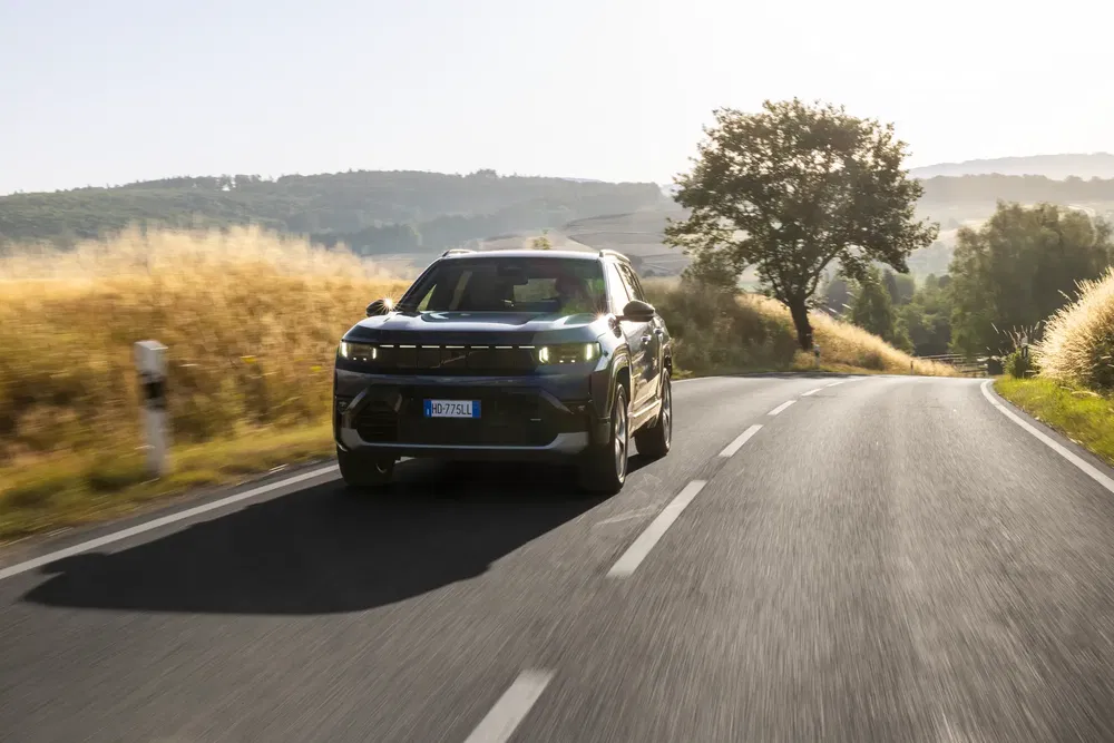 SUV Jeep Avenger roulant sur une route de campagne ensoleillée, entourée de paysages pittoresques.