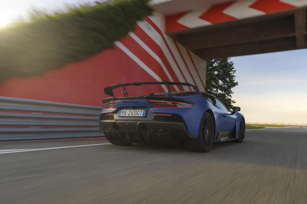 Maserati MC20 bleue sur circuit à grande vitesse, vue arrière avec aileron.