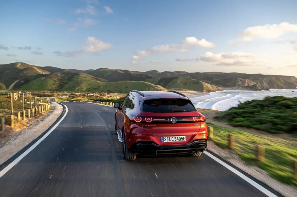 Rode Mercedes EQC SUV op pittoreske kustweg bij zonsondergang.