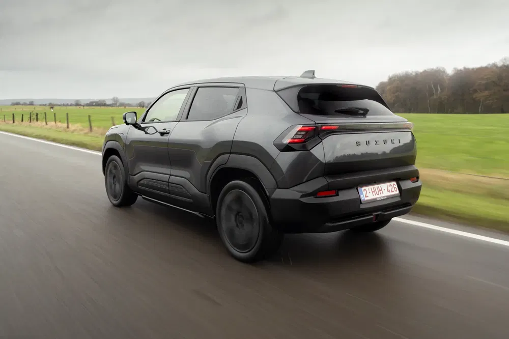 Moderne Suzuki SUV rijdt op een landelijke weg onder bewolkte hemel.