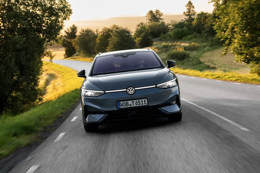 Volkswagen ID.7 roulant sur une route de campagne bordée d'arbres sous la lumière du coucher du soleil.