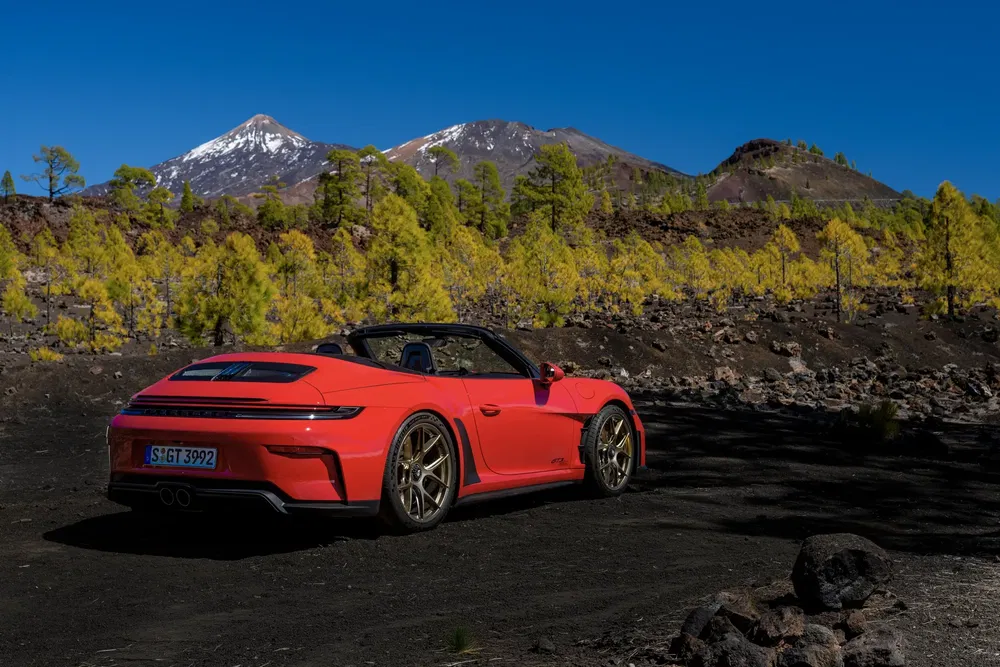 Porsche 911 rouge sur route de montagne avec arbres et montagnes en arrière-plan.