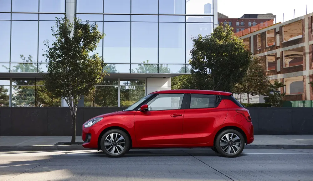 Rode Suzuki Swift geparkeerd voor een modern glazen en stalen gebouw.