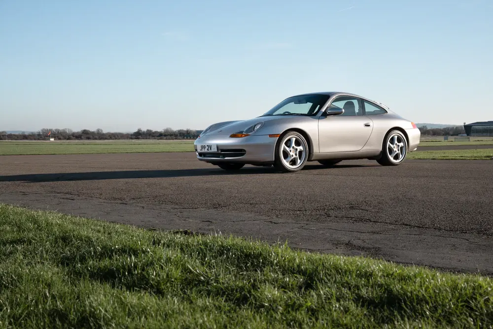 Porsche 911 argentée sur une piste, ciel dégagé en arrière-plan.