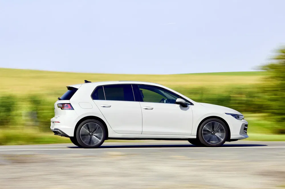 Witte Volkswagen Golf rijdt snel op een landelijke weg, modern en dynamisch design.