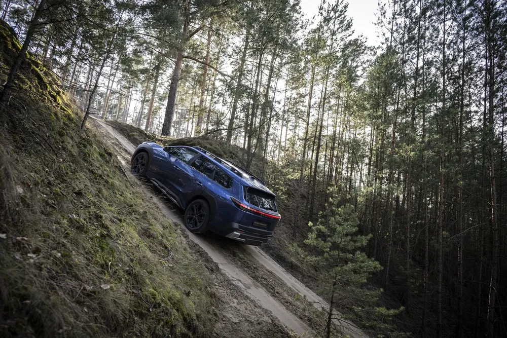 SUV Dacia Duster bleu gravissant une pente escarpée en forêt.