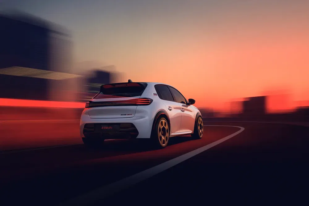 Peugeot 308 GTI blanche sur une route au coucher de soleil, dynamiquement en mouvement.