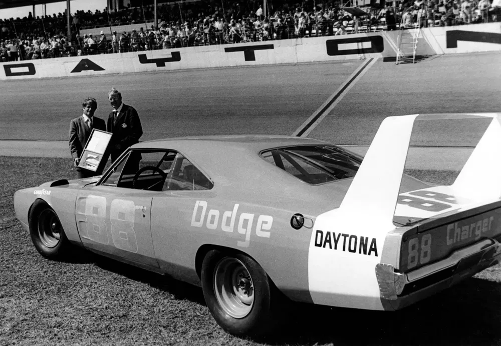 Voiture de course Dodge Charger Daytona n°88 sur circuit NASCAR avec deux hommes en arrière-plan.