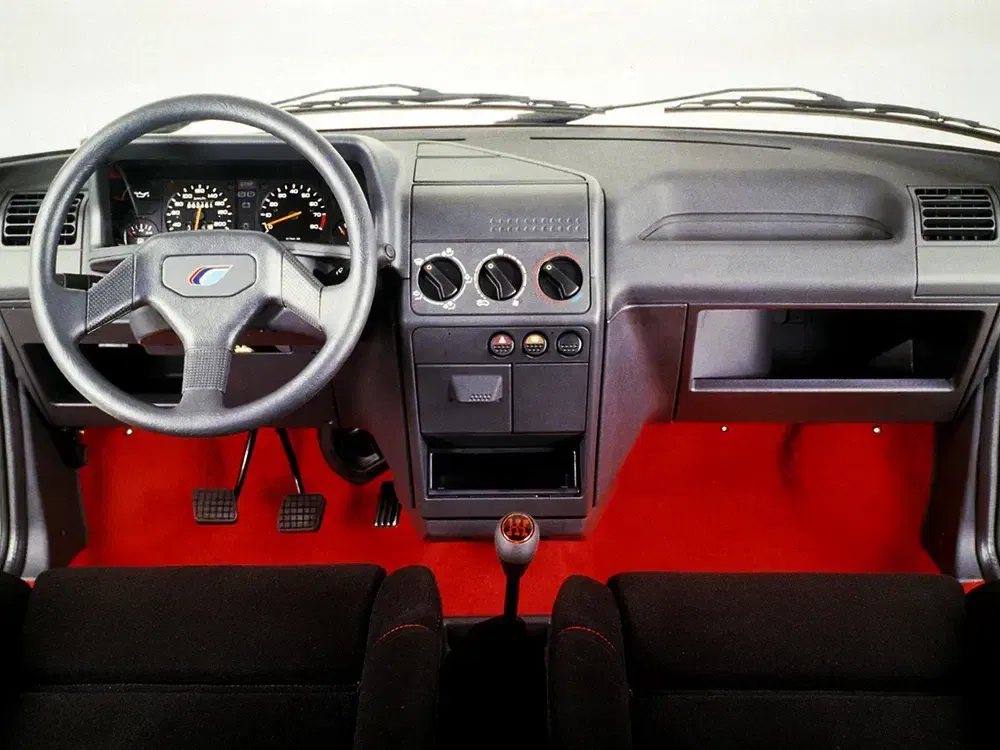 Ouderwets autointerieur met zwart dashboard en felrood tapijt.