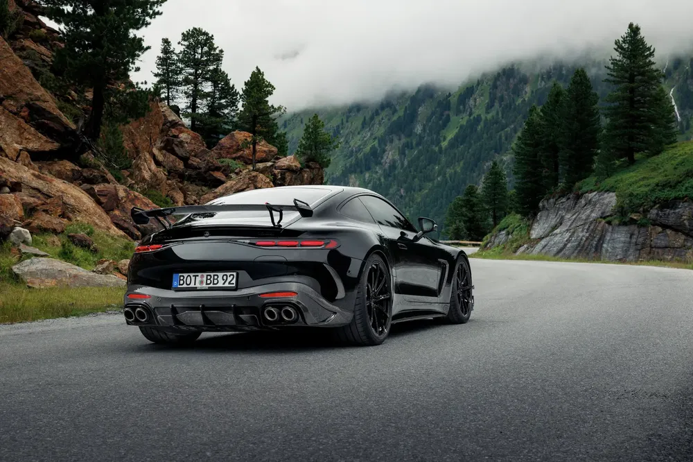Porsche sportive noire sur route de montagne sinueuse entourée de forêts et rochers.