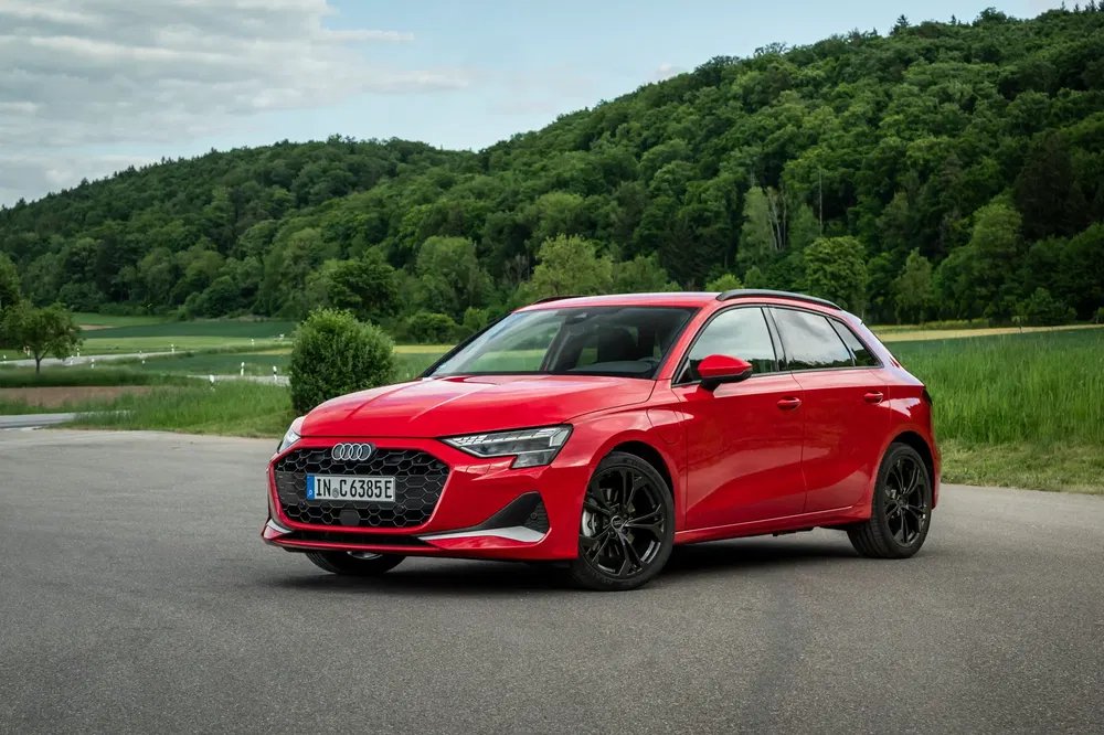 Audi A3 Sportback rouge stationnée devant un paysage verdoyant et collines boisées.