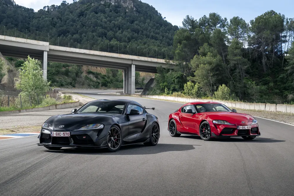 Toyota Supra 2021 zwart en rood op racecircuit met berglandschap.