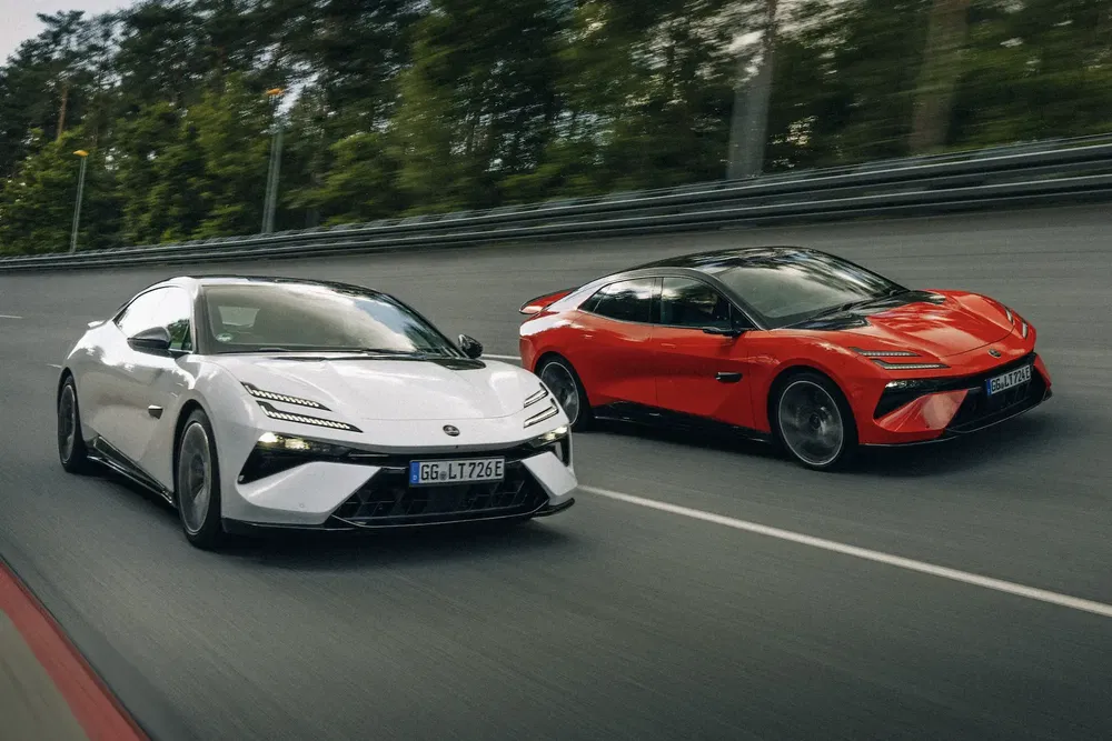 Voitures Lotus Emeya blanches et rouges en course sur une autoroute bordée d'arbres.