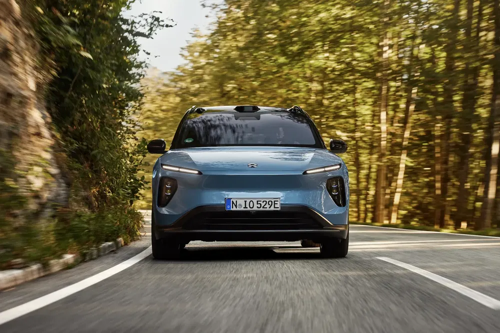 Voiture électrique NIO ES6 bleue roulant sur une route bordée d'arbres durant la journée.