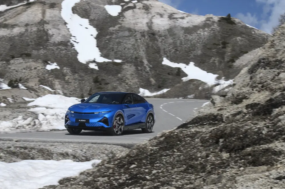 Peugeot 408 bleu sur route montagneuse enneigée, ciel bleu clair.