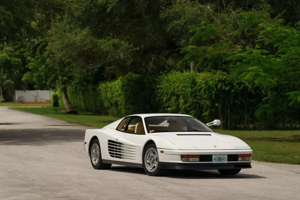 Witte Ferrari Testarossa op een met bomen omzoomde weg, iconisch en sportief design.