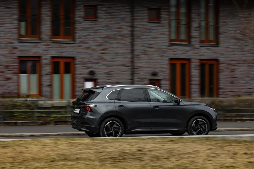 SUV noir roulant devant des bâtiments en briques avec fenêtres en bois.