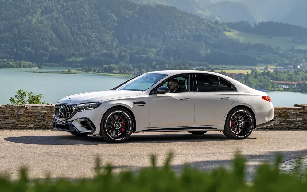 Mercedes Benz AMG blanche surplombant un lac et montagnes verdoyantes en arrière-plan.