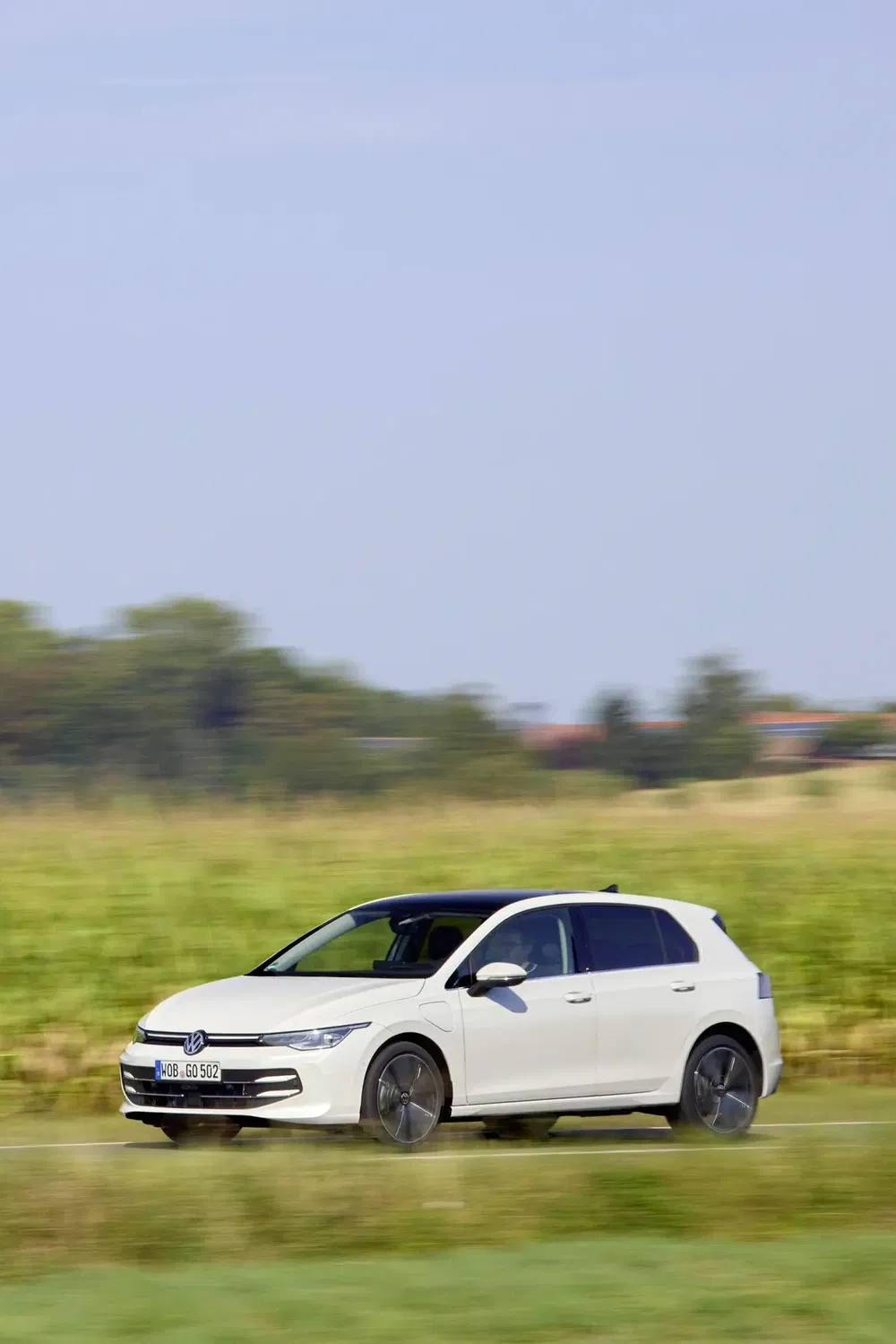 Witte Volkswagen Golf rijdend op een groene landelijke weg.
